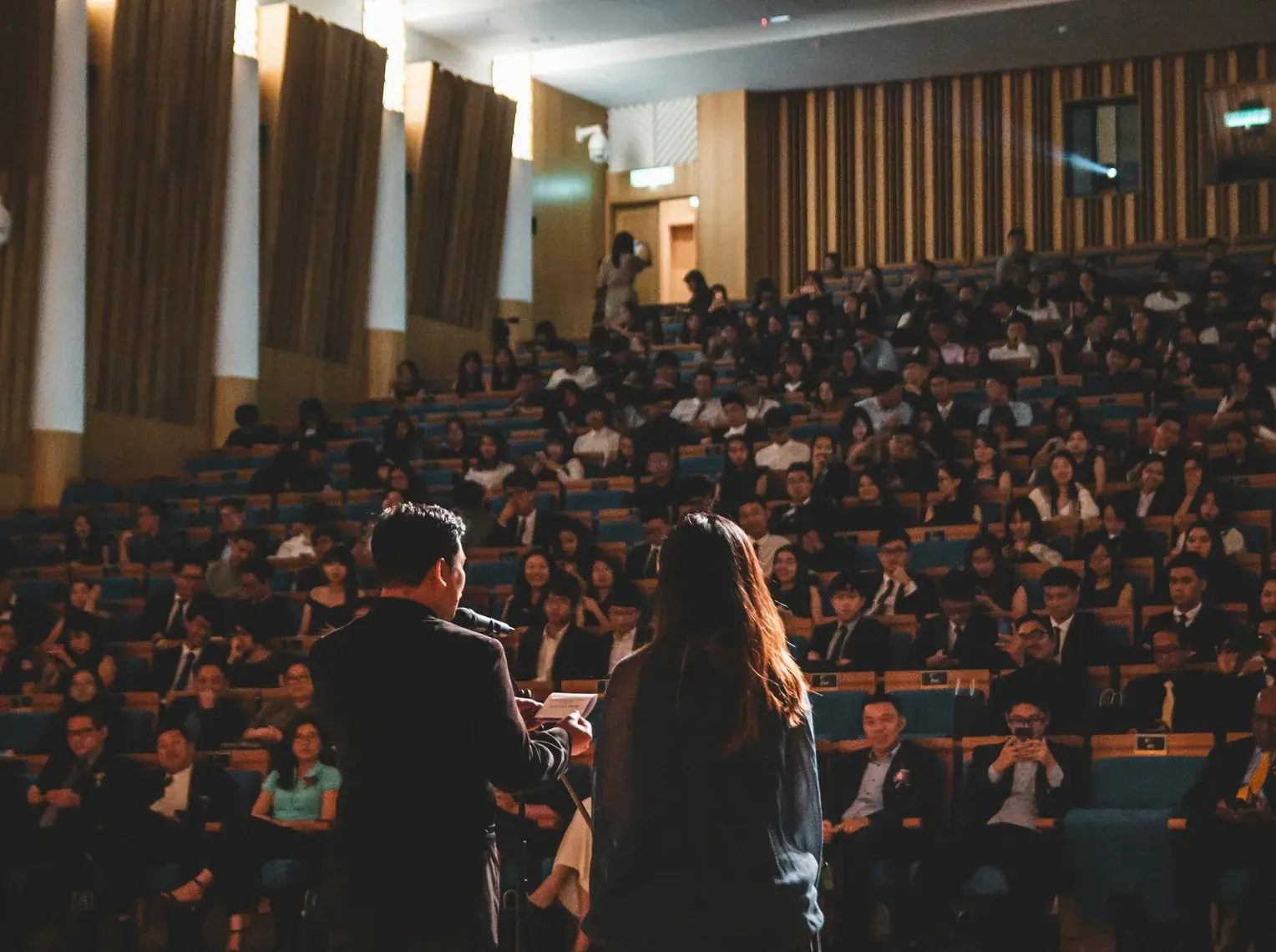 Financial Services — Speakers addressing a full auditorium of formally dressed attendees from the stage